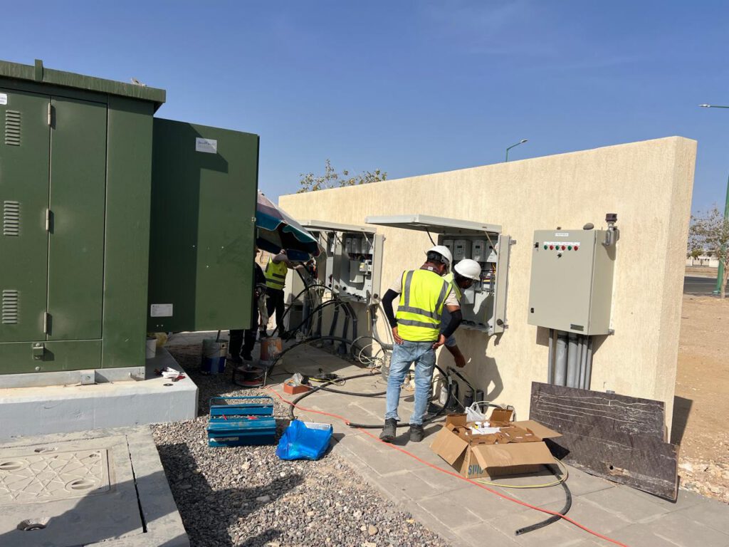 Technicians terminating cables into wall mounted distribution boards beside a kiosk substation