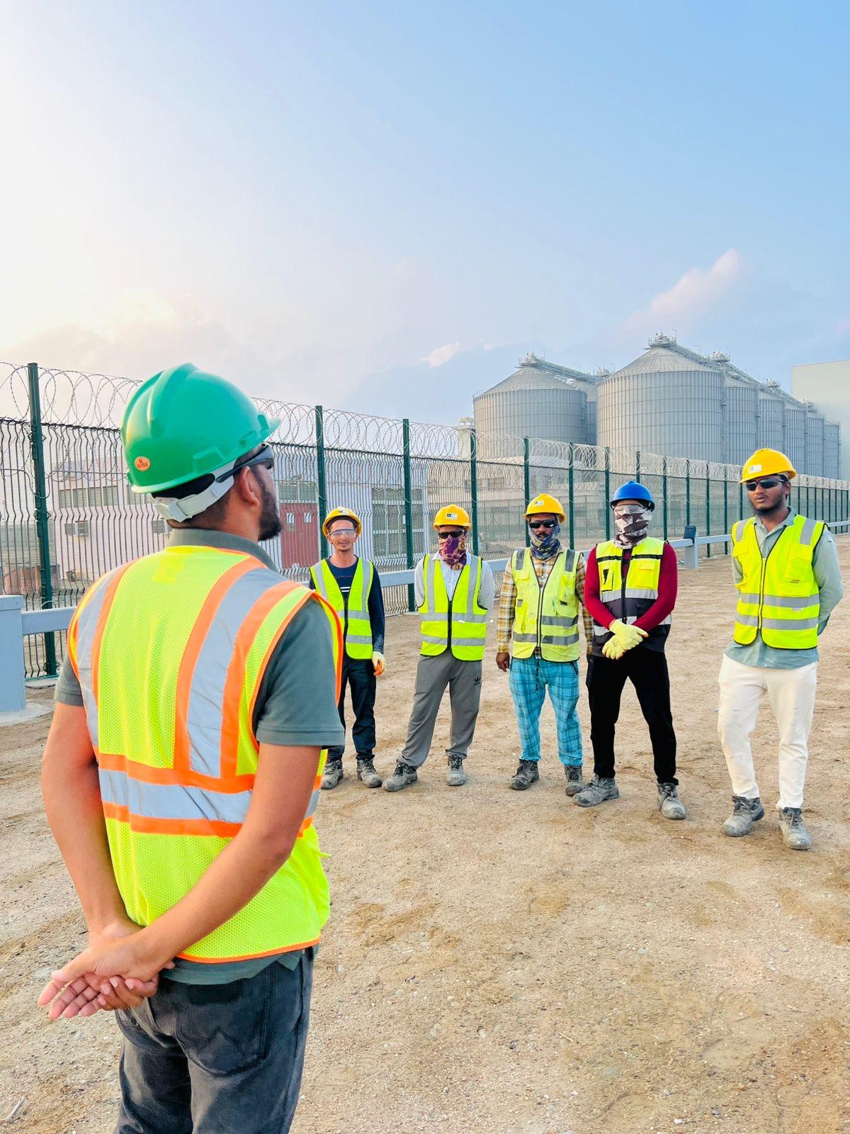SFAA site supervisor briefing a crew in high visibility vests at first light, storage silos behind